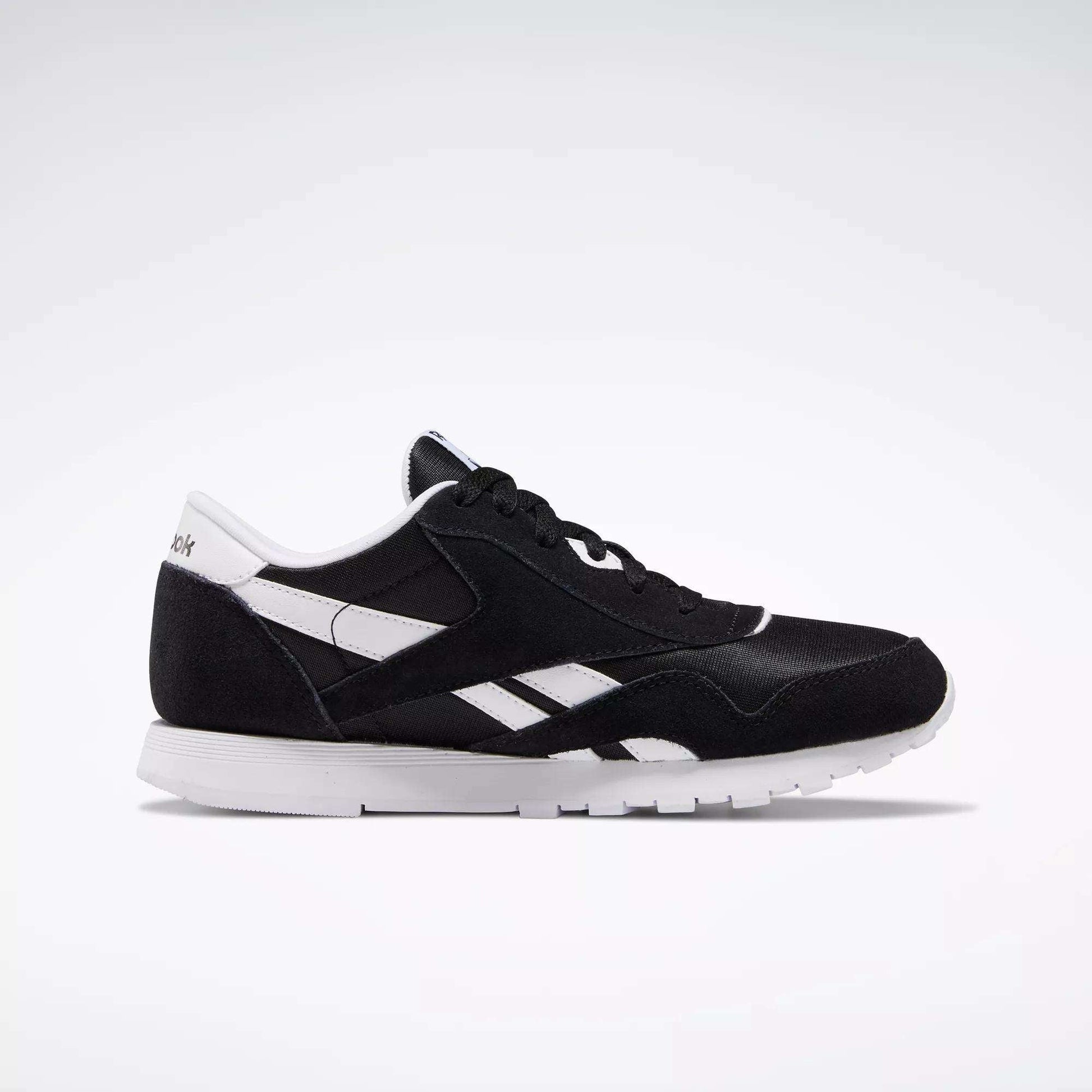 The Reebok Classic Nylon Shoes - Big Kids feature a black and white 80s-inspired minimalist design with side stripes, branding, and a white sole, shown in profile against a light background.