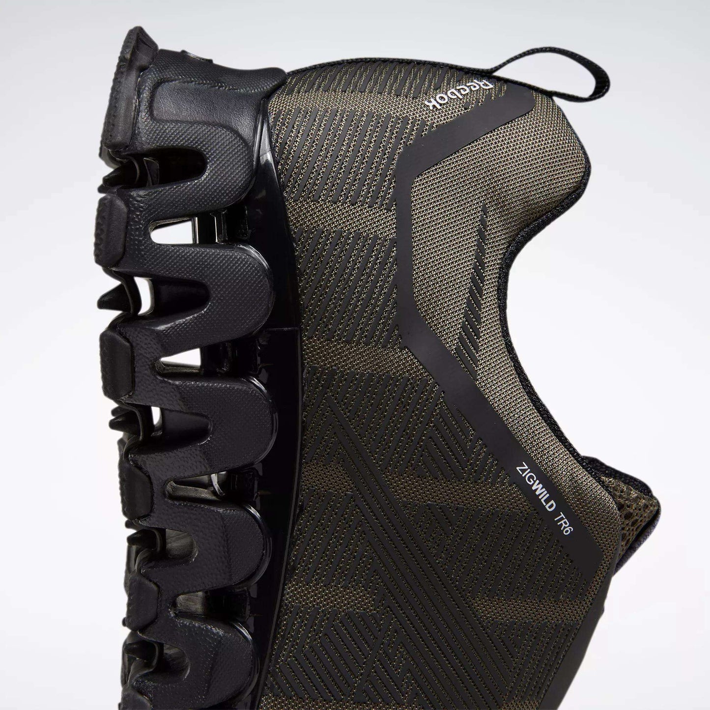 A close-up side view of the Reebok Men's ZigWild Trail 6 Shoes in black, highlighting the unique zigzag-shaped sole for cushioning and a textured upper, set against a light background.