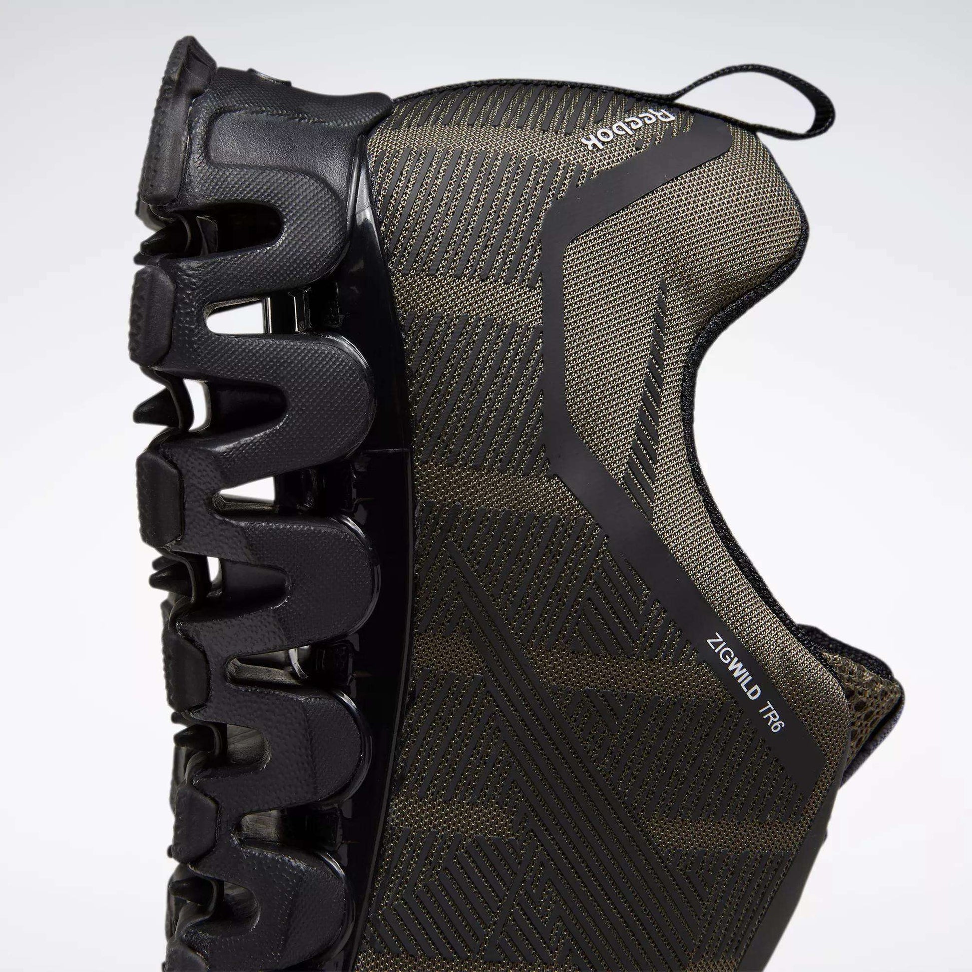 A close-up side view of the Reebok Men's ZigWild Trail 6 Shoes in black, highlighting the unique zigzag-shaped sole for cushioning and a textured upper, set against a light background.