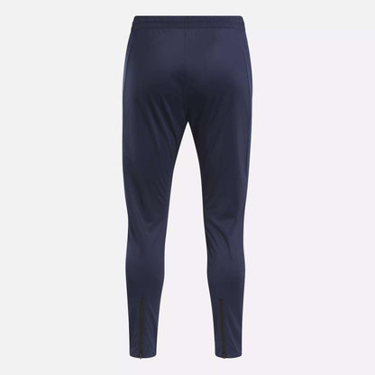 The Reebok Men's Workout Ready Track Pant in navy blue features a slim fit, elastic waistband, and ankle zippers—ideal as workout pants for any training session. Shown from the back.