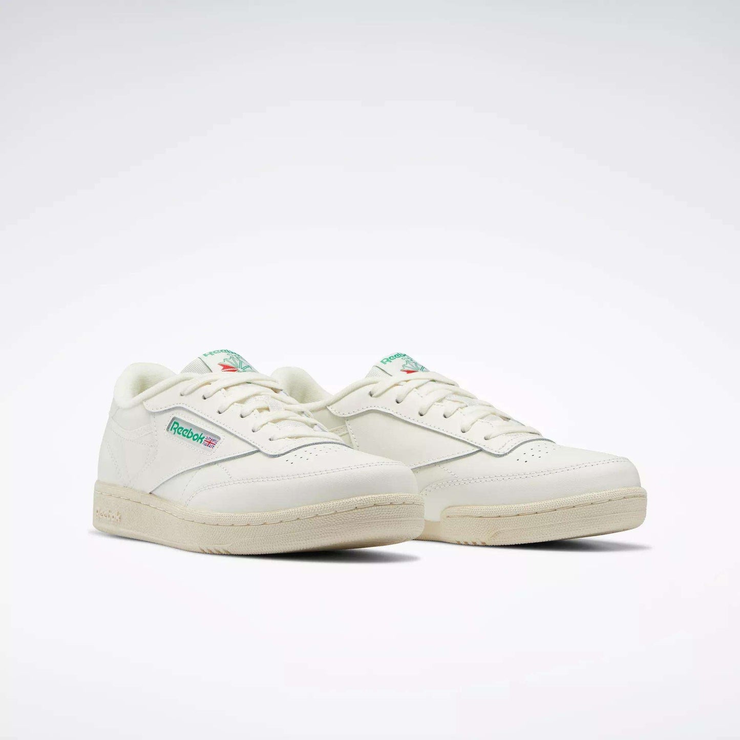 The Reebok Club C Shoes for big kids feature an off-white design with green and red logo details on the side and tongue, inspired by classic '80s style, set against a plain white background.
