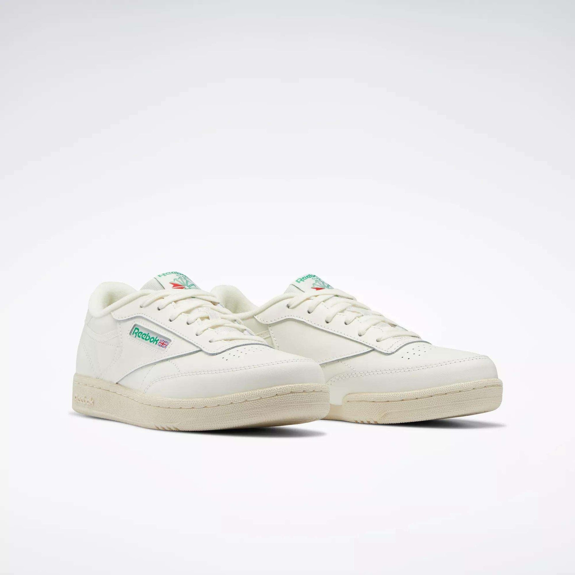 The Reebok Club C Shoes for big kids feature an off-white design with green and red logo details on the side and tongue, inspired by classic '80s style, set against a plain white background.