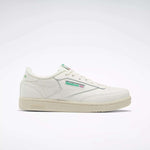 The Reebok Club C Shoes - Big Kids feature a white upper, green and red logo accents, beige sole, and classic low-top '80s style. Shown in profile on a light background, they're perfect for junior boys wanting timeless Reebok sneakers.