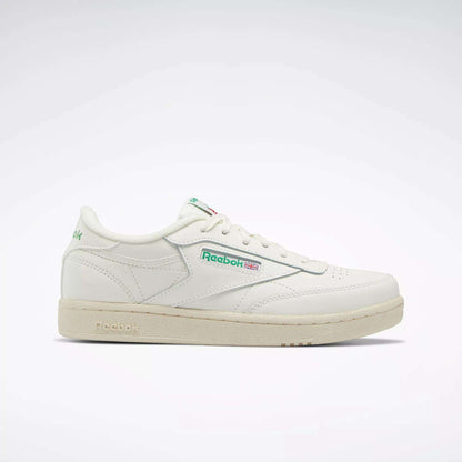 The Reebok Club C Shoes - Big Kids feature a white upper, green and red logo accents, beige sole, and classic low-top '80s style. Shown in profile on a light background, they're perfect for junior boys wanting timeless Reebok sneakers.