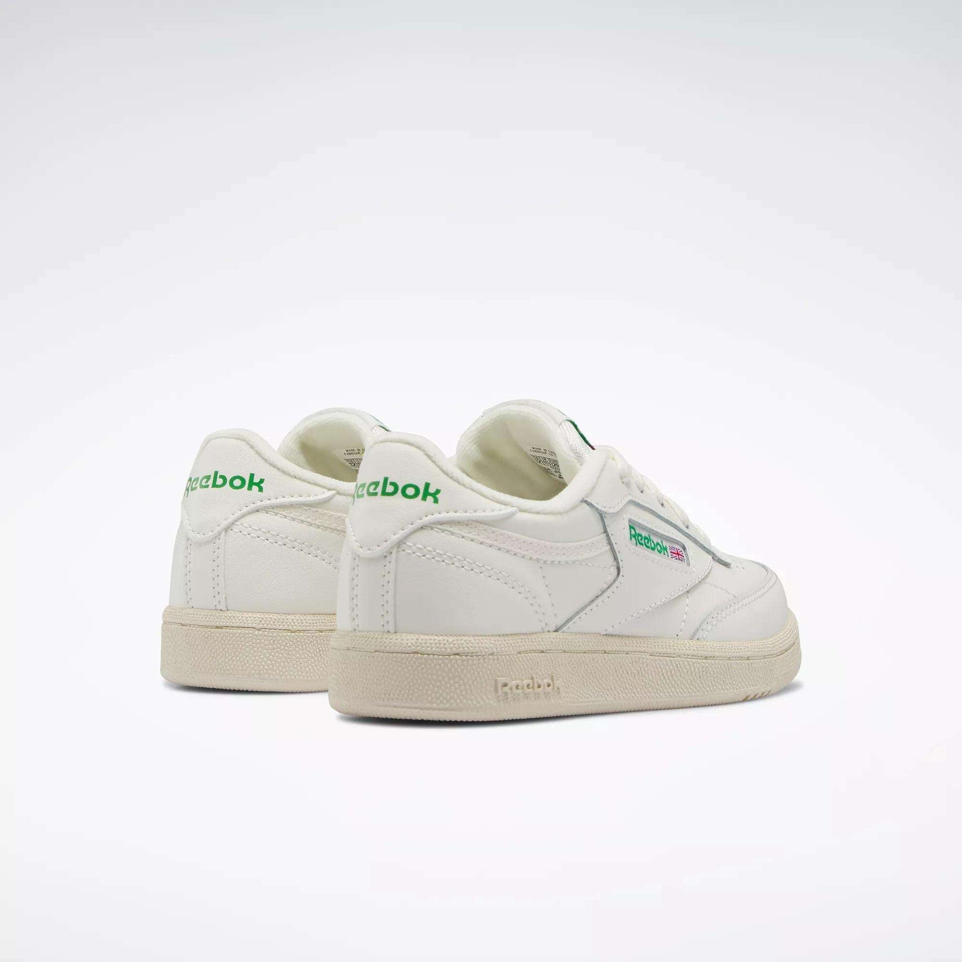 The Reebok Kids' Club C Shoes - Preschool feature white uppers with green accents and beige soles, classic '80s style, and visible Reebok logos on the side and heel—an ideal retro-inspired choice for boys shown on a plain light background.