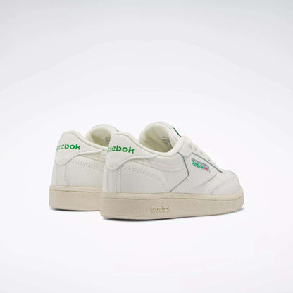 The Reebok Kids' Club C Shoes - Preschool feature white uppers with green accents and beige soles, classic '80s style, and visible Reebok logos on the side and heel—an ideal retro-inspired choice for boys shown on a plain light background.