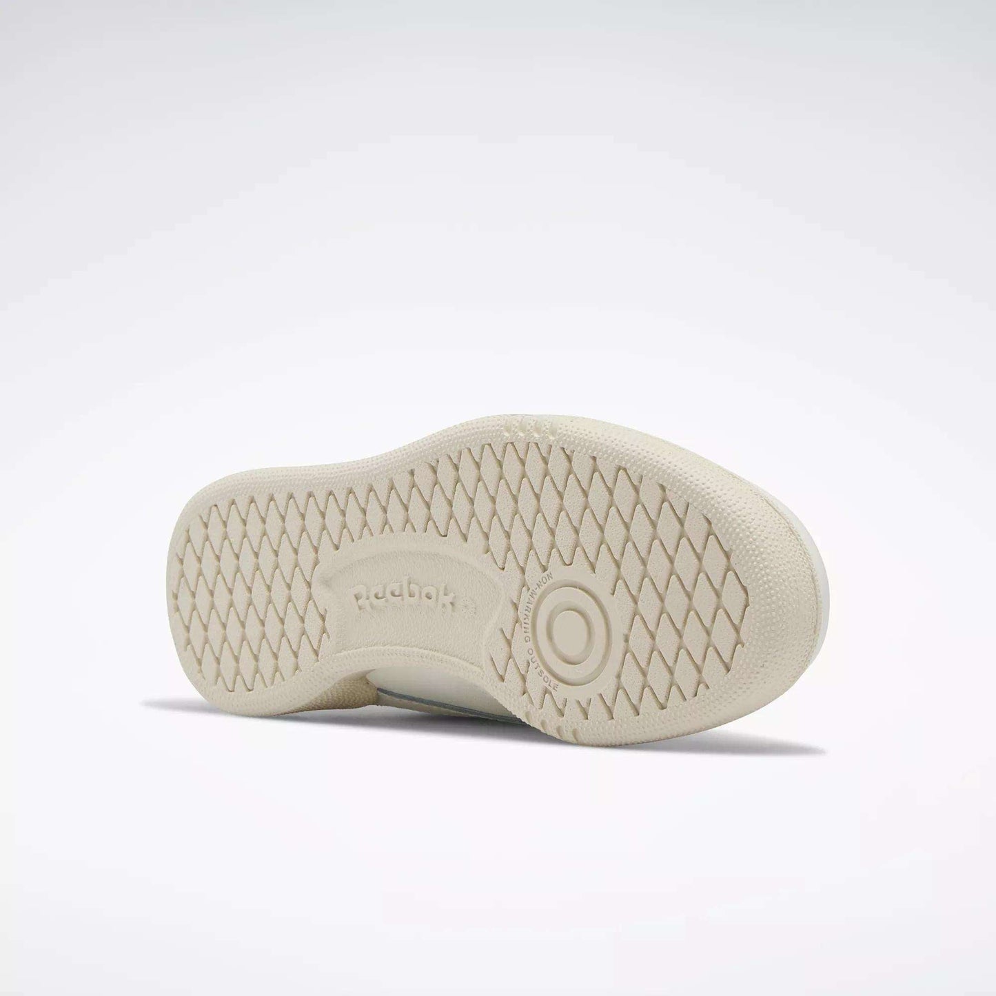 The image shows the sole of a beige Reebok Kids' Club C Shoe - Preschool with a diamond-patterned tread and the Reebok logo at the center. The clean sole and classic style evoke '80s vibes, with the shoe lying on its side against a plain background.
