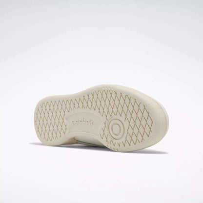 The image shows the sole of a beige Reebok Kids' Club C Shoe - Preschool with a diamond-patterned tread and the Reebok logo at the center. The clean sole and classic style evoke '80s vibes, with the shoe lying on its side against a plain background.