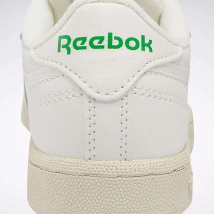 Close-up of the back of a white Reebok Kids' Club C Shoe for preschoolers, featuring "Reebok" in green on the heel tab, textured off-white soles, and detailed stitching inspired by '80s style.