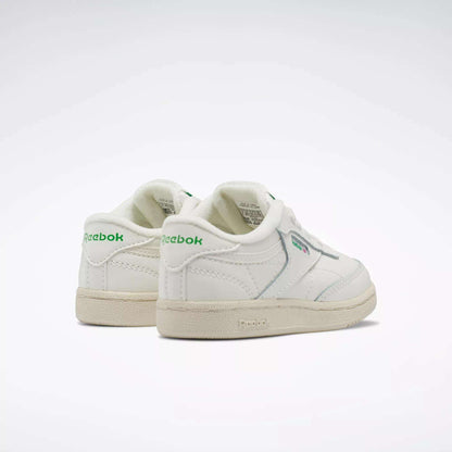 A pair of Reebok Kids' Club C Shoes for babies and toddlers with green logo accents, off-white soles, and an iconic ’80s low-top style. Positioned side by side on a white background, these sneakers add a retro touch.