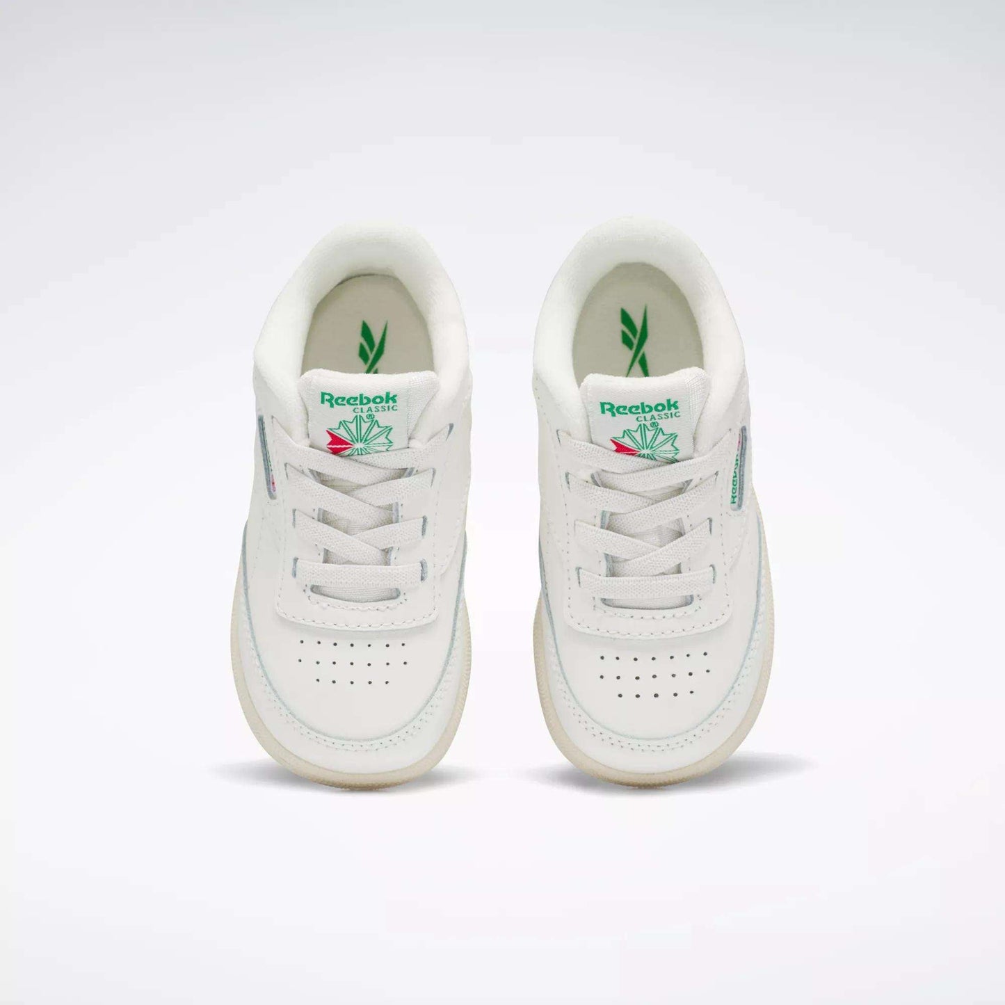 A pair of Reebok Kids' Club C Shoes for toddlers in white with green and pink accents, inspired by '80s style, shown from above on a plain background. Both shoes feature the Reebok logo and a leaf graphic on the tongue.