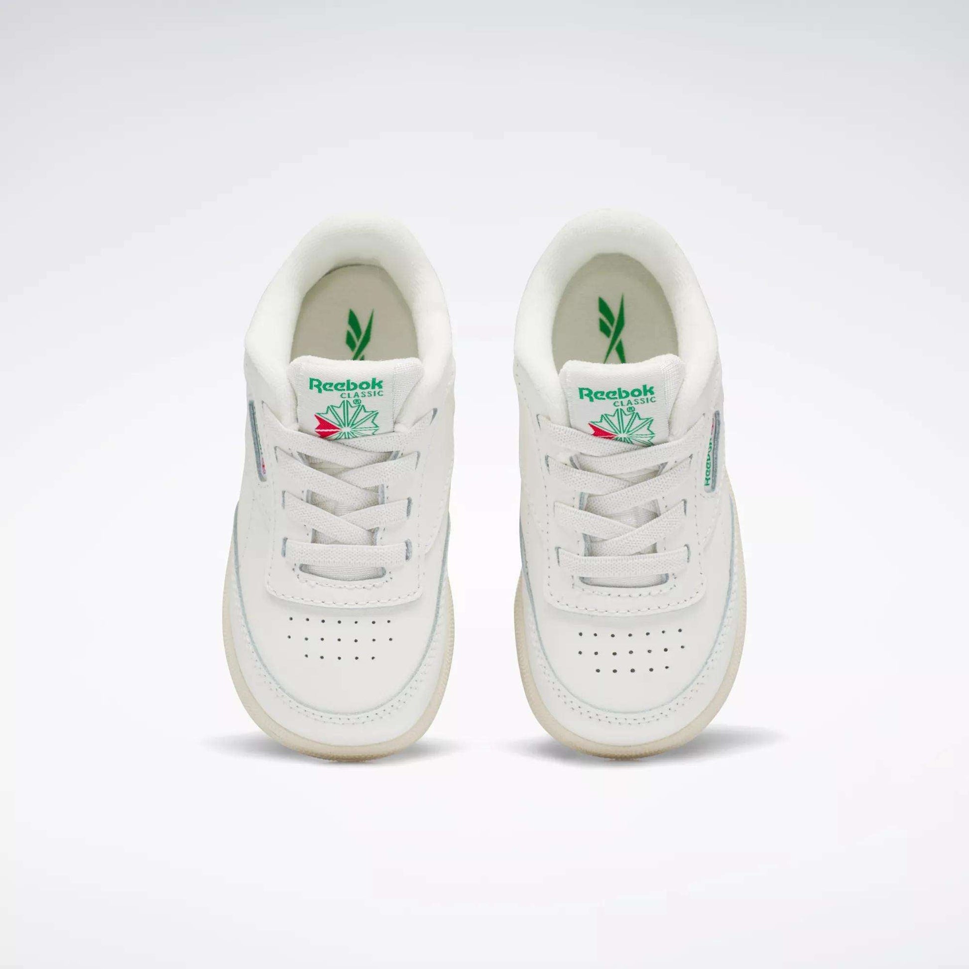 A pair of Reebok Kids' Club C Shoes for toddlers in white with green and pink accents, inspired by '80s style, shown from above on a plain background. Both shoes feature the Reebok logo and a leaf graphic on the tongue.