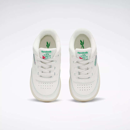 A pair of Reebok Kids' Club C Shoes for toddlers in white with green and pink accents, inspired by '80s style, shown from above on a plain background. Both shoes feature the Reebok logo and a leaf graphic on the tongue.