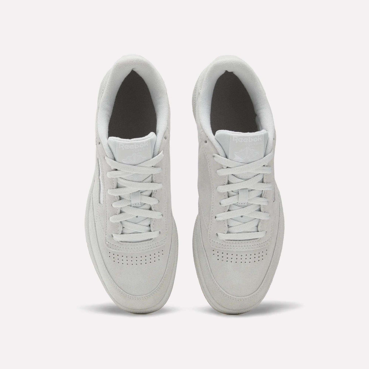 A top-down view of Reebok Club C 85 Shoes in white, showcasing clean laces, a suede upper, toe perforations, and light gray soles on a plain white background.