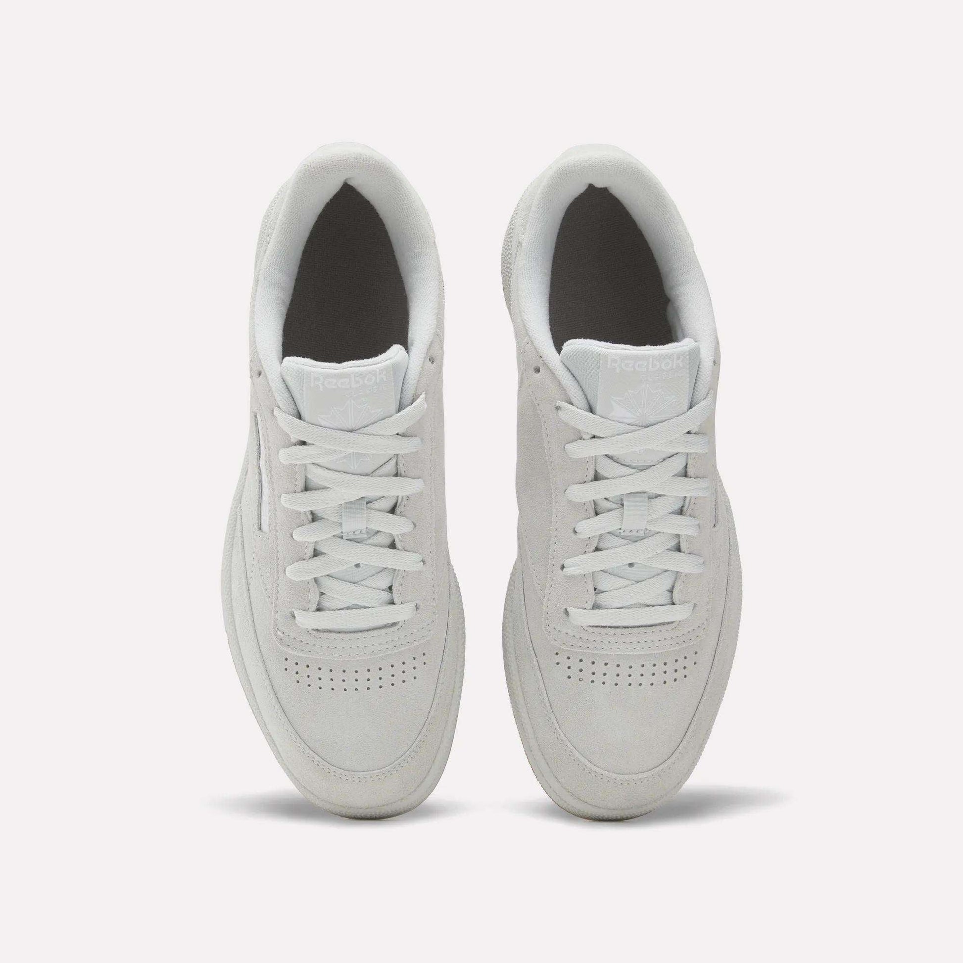 A top-down view of Reebok Club C 85 Shoes in white, showcasing clean laces, a suede upper, toe perforations, and light gray soles on a plain white background.