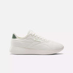 The Reebok Active Lite Shoes are white minimalist sneakers with a low profile, white laces, a textured sole, green heel accent, and a breathable upper for all-day comfort. Shown on a plain white background.