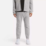 A person in a light gray zip-up jacket and Reebok Men's Active Collective DreamBlend Pants with white sneakers stands against a plain light background; their face is not visible.