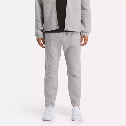 A person in a light gray zip-up jacket and Reebok Men's Active Collective DreamBlend Pants with white sneakers stands against a plain light background; their face is not visible.