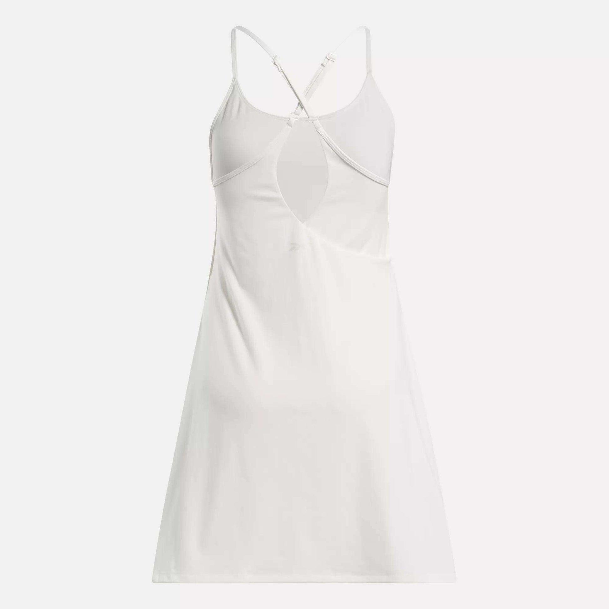 The Reebok Women's Lux Strappy Dress is a sporty, sleeveless white dress with thin crisscross adjustable back straps and a keyhole cutout below the shoulder blades, shown on a plain white background.