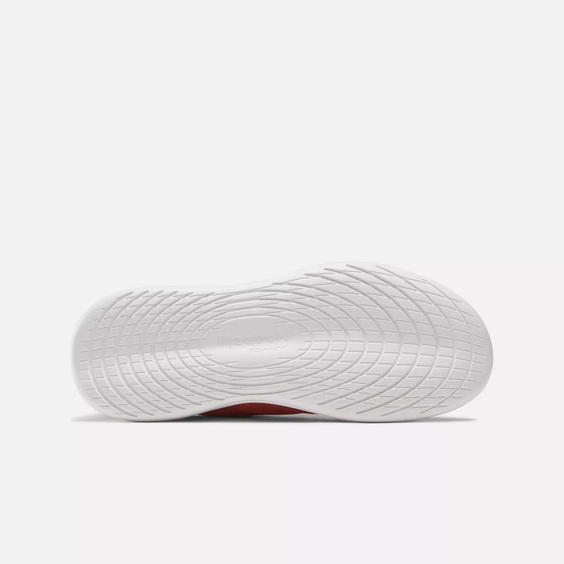 The image shows the bottom view of a Women's Active Lite Shoe sole by Reebok, featuring a textured wavy grip pattern. The Reebok name is embossed at the center. The minimalist sneaker is set against a plain, light-colored background.