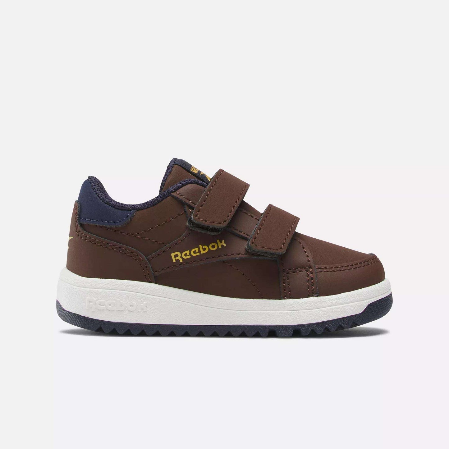 The Weebok Clasp Low Shoes by Reebok feature a brown design with navy accents, a Velcro strap, white sole, and gold Reebok logo—perfect for infants and toddlers’ daily wear. Shown on a white background.