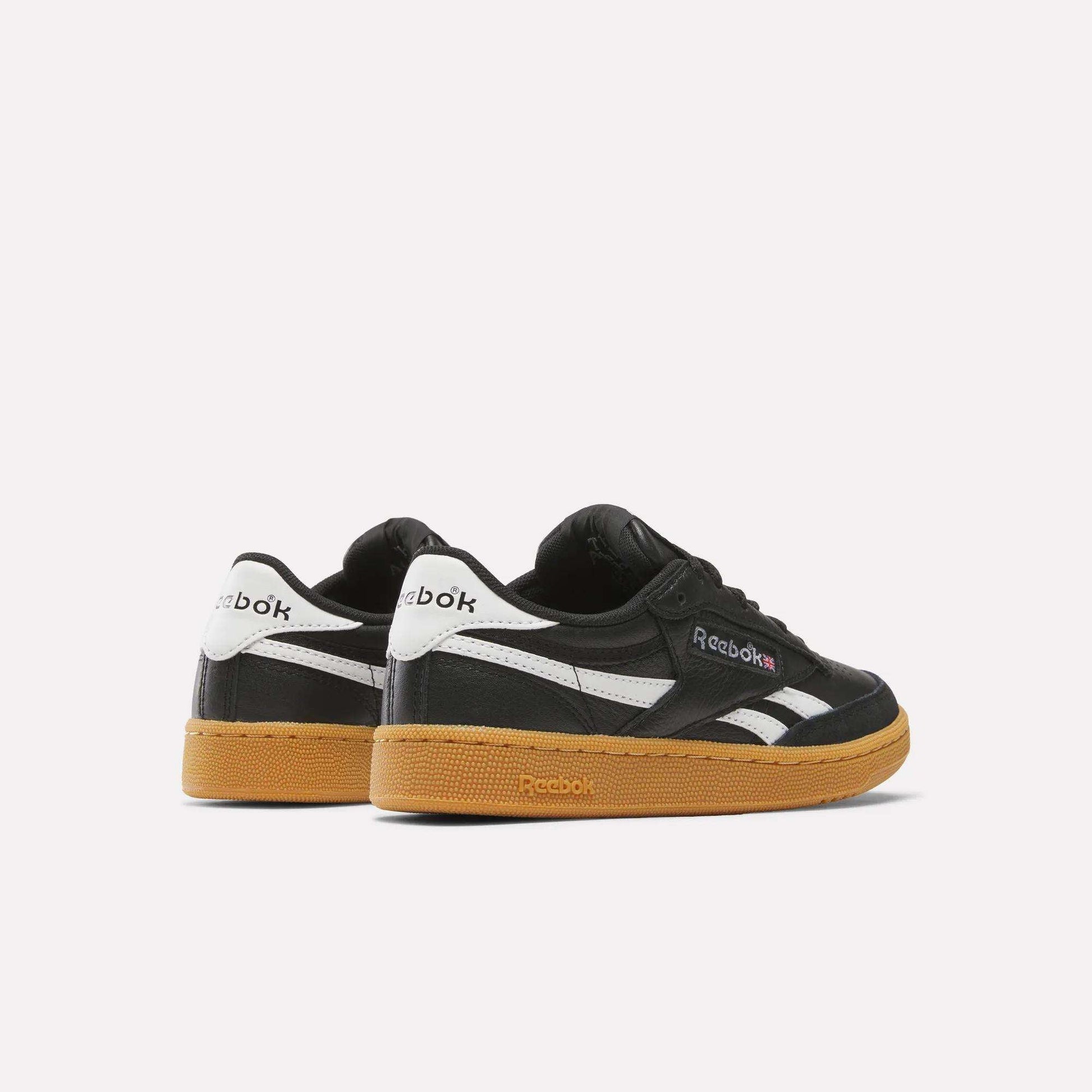 A pair of Reebok Club C Revenge Vintage Shoes in black with white accents and a brown gum sole are displayed on a plain white background. One shoe faces forward, while the other is angled to display the back.