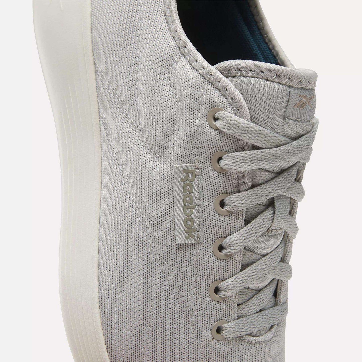 Close-up of light gray Reebok Active Lite Shoes, featuring a minimalist lace-up design, textured fabric, stitched details, and a Reebok tag. The white sole adds to the clean look and lightweight feel of these sneakers.