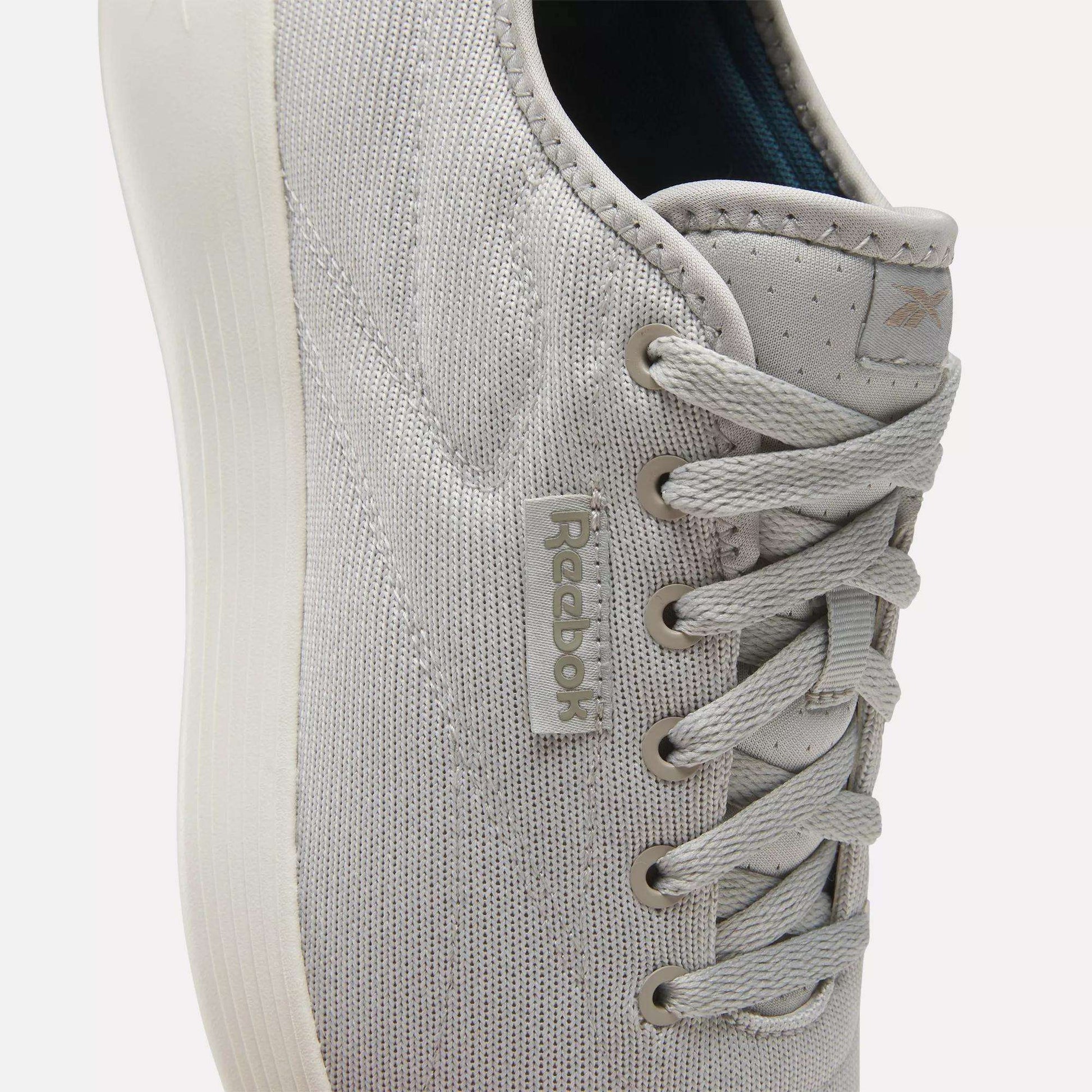 Close-up of light gray Reebok Active Lite Shoes, featuring a minimalist lace-up design, textured fabric, stitched details, and a Reebok tag. The white sole adds to the clean look and lightweight feel of these sneakers.
