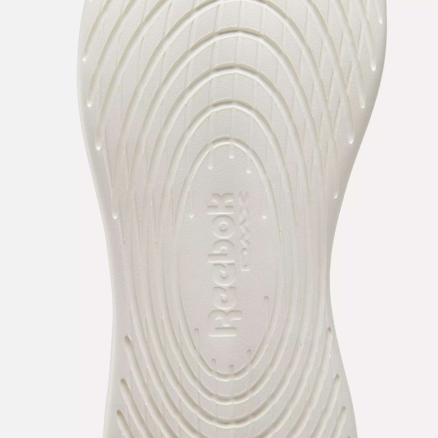 Close-up of the white sole on Reebok Active Lite Shoes, showcasing concentric oval grooves and embossed "Reebok" branding at the center.