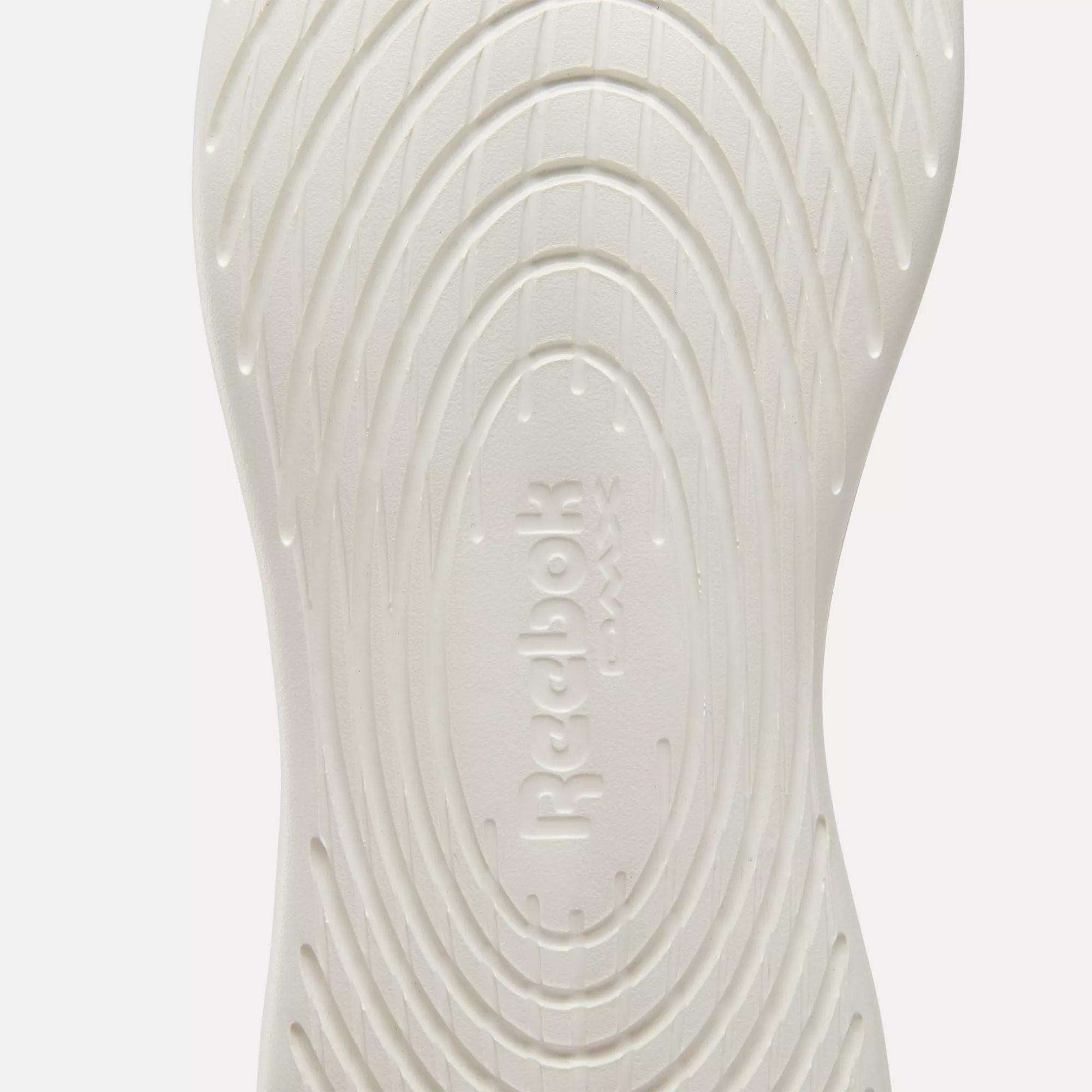 Close-up of the white sole on Reebok Active Lite Shoes, showcasing concentric oval grooves and embossed "Reebok" branding at the center.