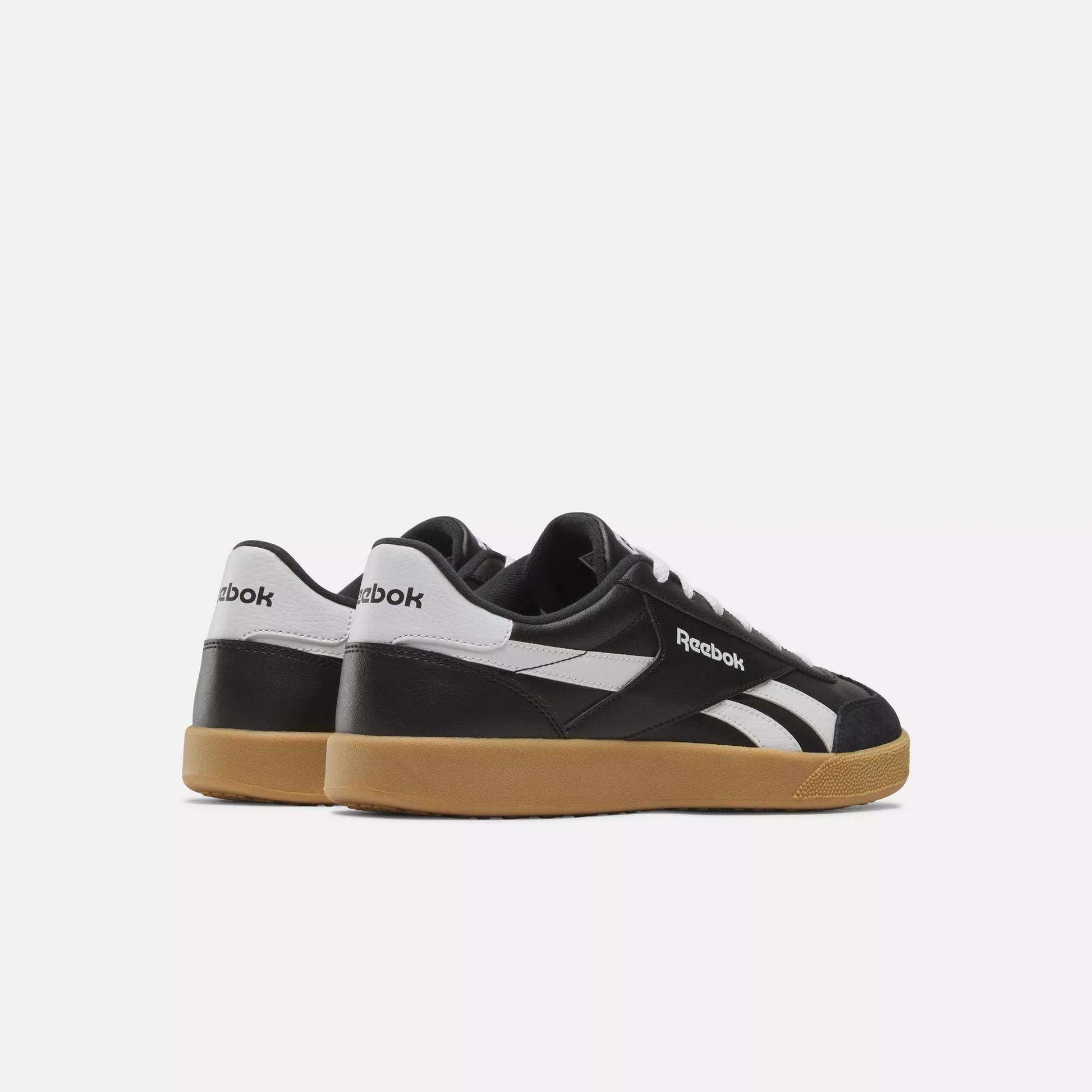 The Reebok Smash Edge Shoes feature a minimalist black-and-white design with gum-colored soles, inspired by classic court style, shown from the back and side on a plain white background.