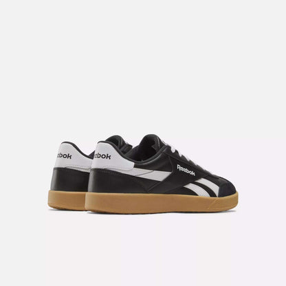 The Reebok Smash Edge Shoes feature a minimalist black-and-white design with gum-colored soles, inspired by classic court style, shown from the back and side on a plain white background.