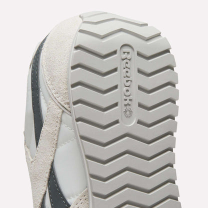 Close-up of the sole on Women's Classic AZ Shoes by Reebok, highlighting the zigzag tread and embossed Reebok logo. These vintage sneakers come in light gray and beige.