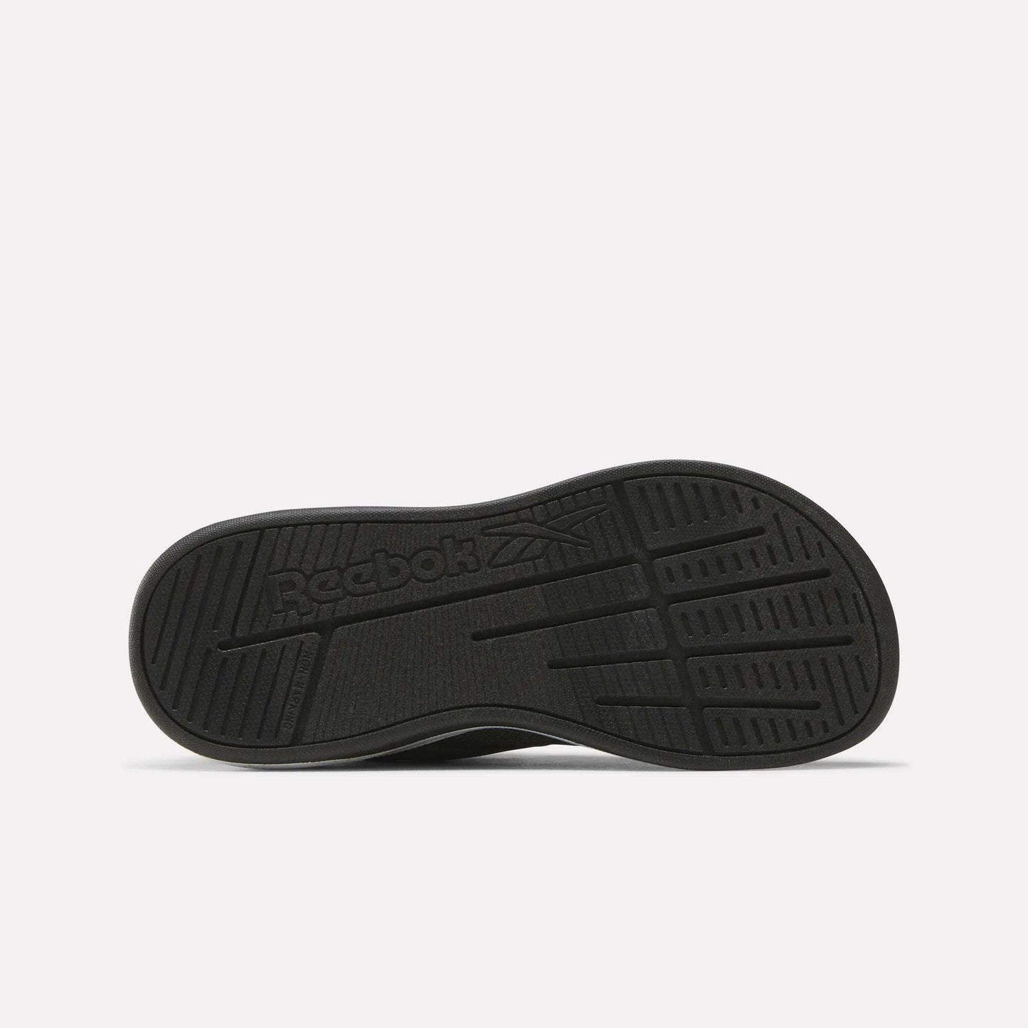 The image shows the black rubber outsole of the Reebok Nano Play Stretch Lace And Top Strap Shoes for little kids, with textured grip patterns and an embossed Reebok logo featuring the brand's vector symbol in the center.