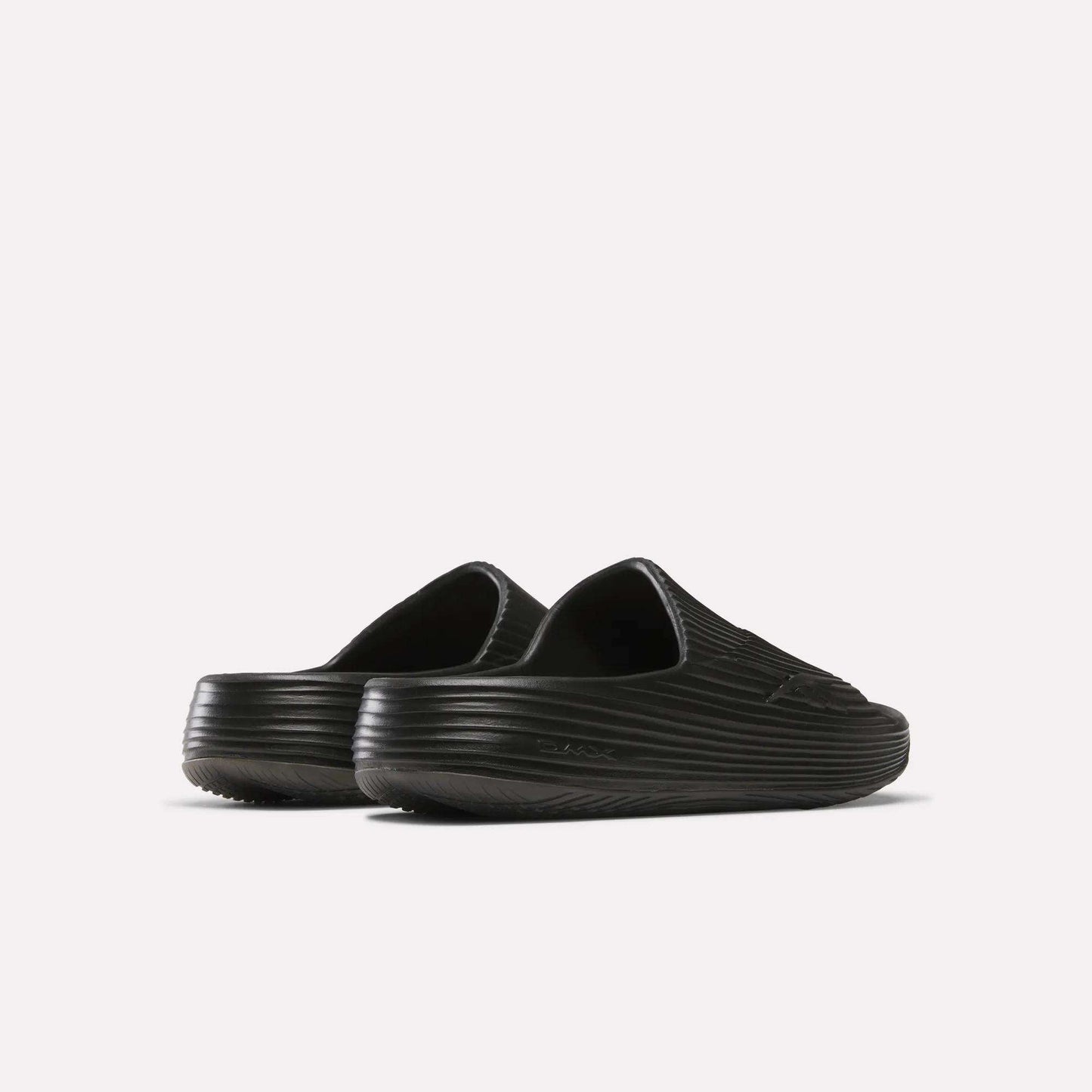 The Reebok DMX Recovery Walking Slides are black slip-on clogs with a ribbed texture, closed toes, and super-soft foam for extra comfort, shown from the back and side on a plain white background.
