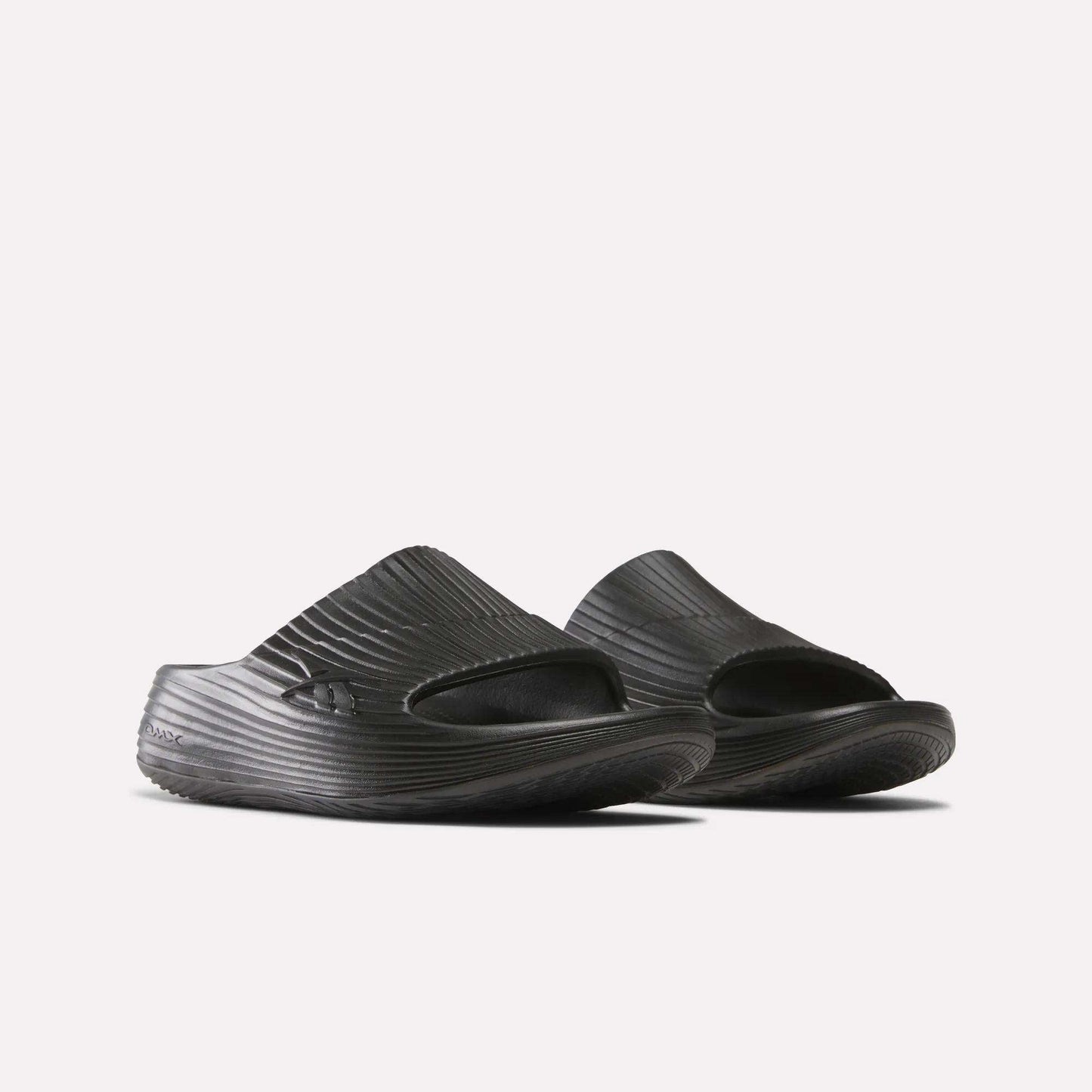 A pair of Reebok DMX Recovery Walking Slides in black, featuring textured ridged surfaces, open toes, and super-soft foam for comfort, shown side by side on a white background.