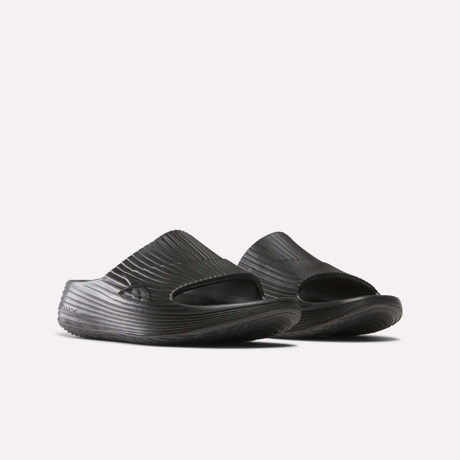 A pair of Reebok DMX Recovery Walking Slides in black, featuring textured ridged surfaces, open toes, and super-soft foam for comfort, shown side by side on a white background.