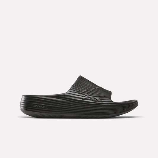A single Reebok DMX Recovery Walking Slide in black, featuring a textured ridged design, thick sole, super-soft foam, and open toe, is displayed against a plain white background.