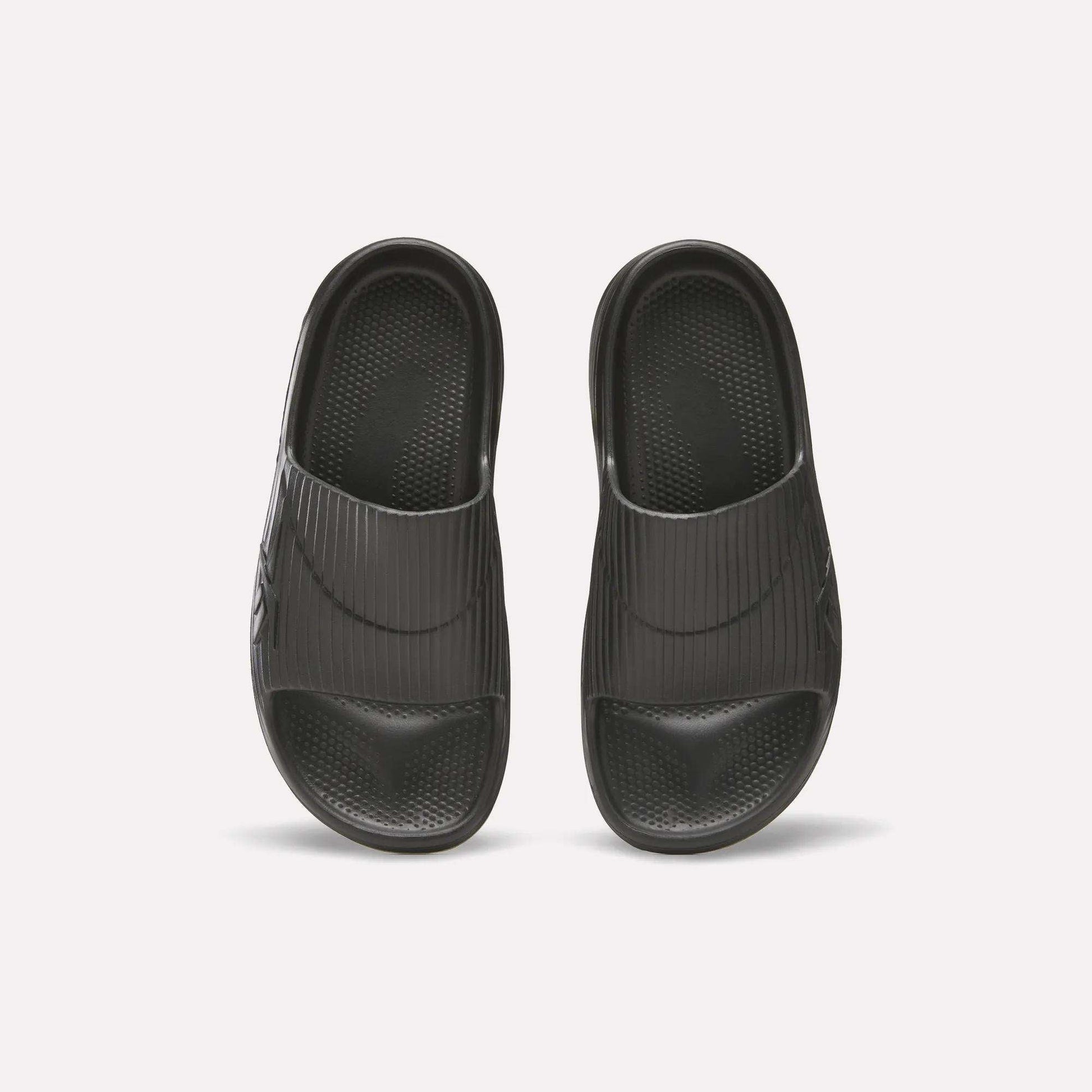 Reebok DMX Recovery Walking Slides in black, shown from above on a white background; feature wide ribbed straps, textured footbeds, and ultra-soft foam for comfort.