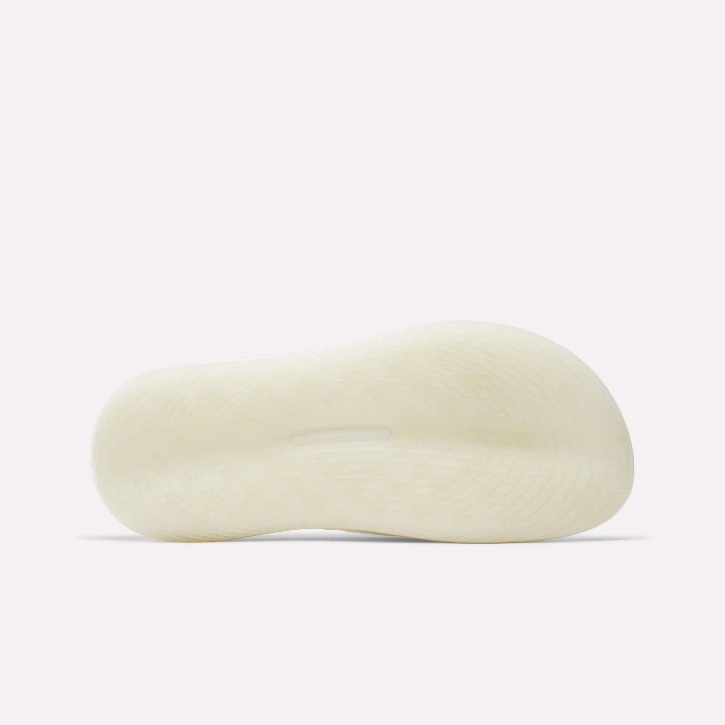 The image shows the bottom view of a Reebok DMX Recovery Walking Slide in white or light beige, highlighting its textured sole with a slightly raised arch. The background is plain and light-colored.
