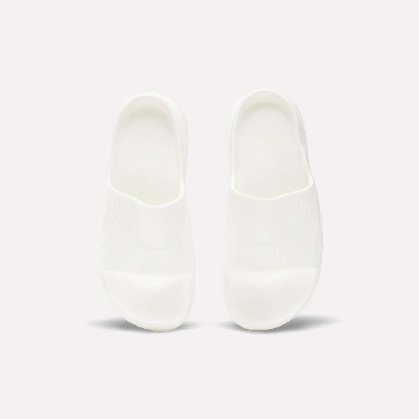 A pair of Reebok DMX Recovery Walking Slides in plain white are placed side by side on a light background, viewed from above.