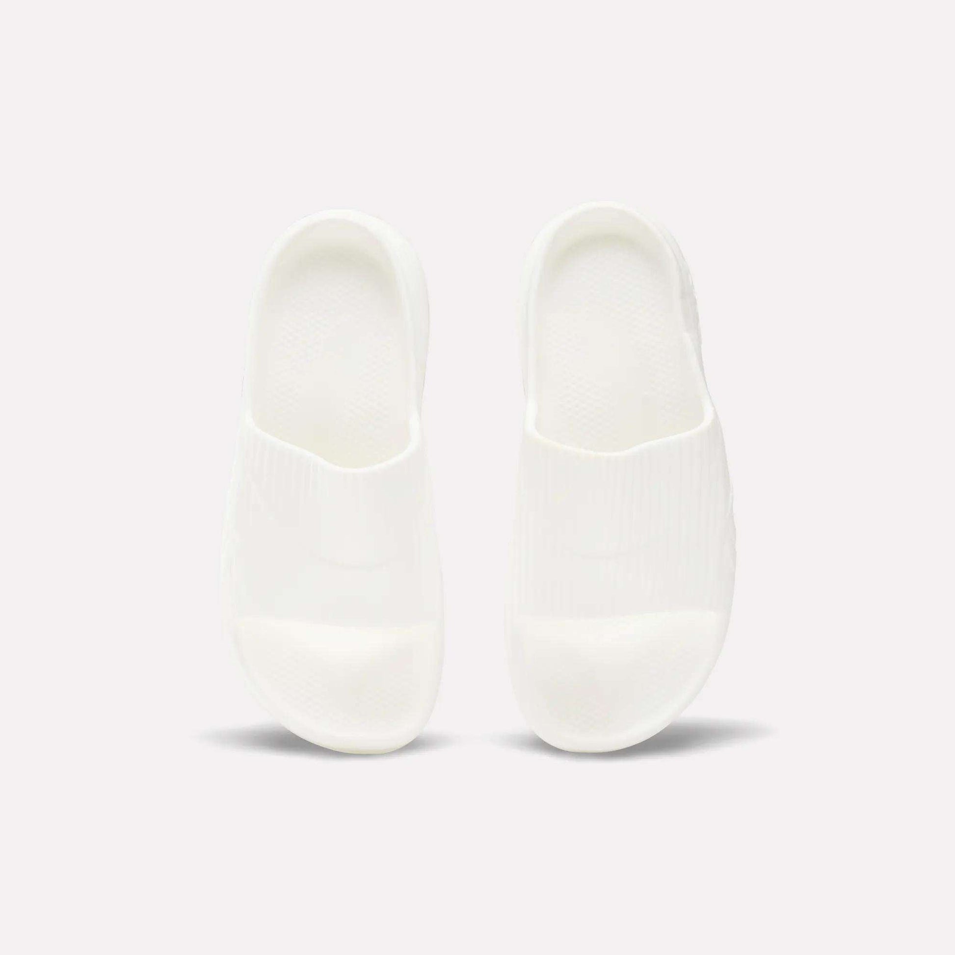 A pair of Reebok DMX Recovery Walking Slides in plain white are placed side by side on a light background, viewed from above.