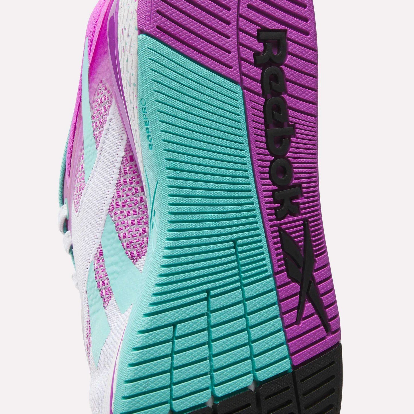 Close-up of the sole of Reebok Women's Nano X5 Training Shoes, showing textured grip patterns in pink, teal, and black, with the “Reebok” name and logo clearly visible.