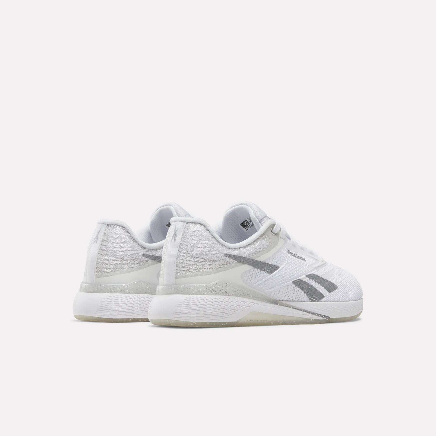 A pair of Reebok Women's Nano X5 Training Shoes, featuring a white design with gray accents and textured details, is positioned on a white surface to display the back and side views.