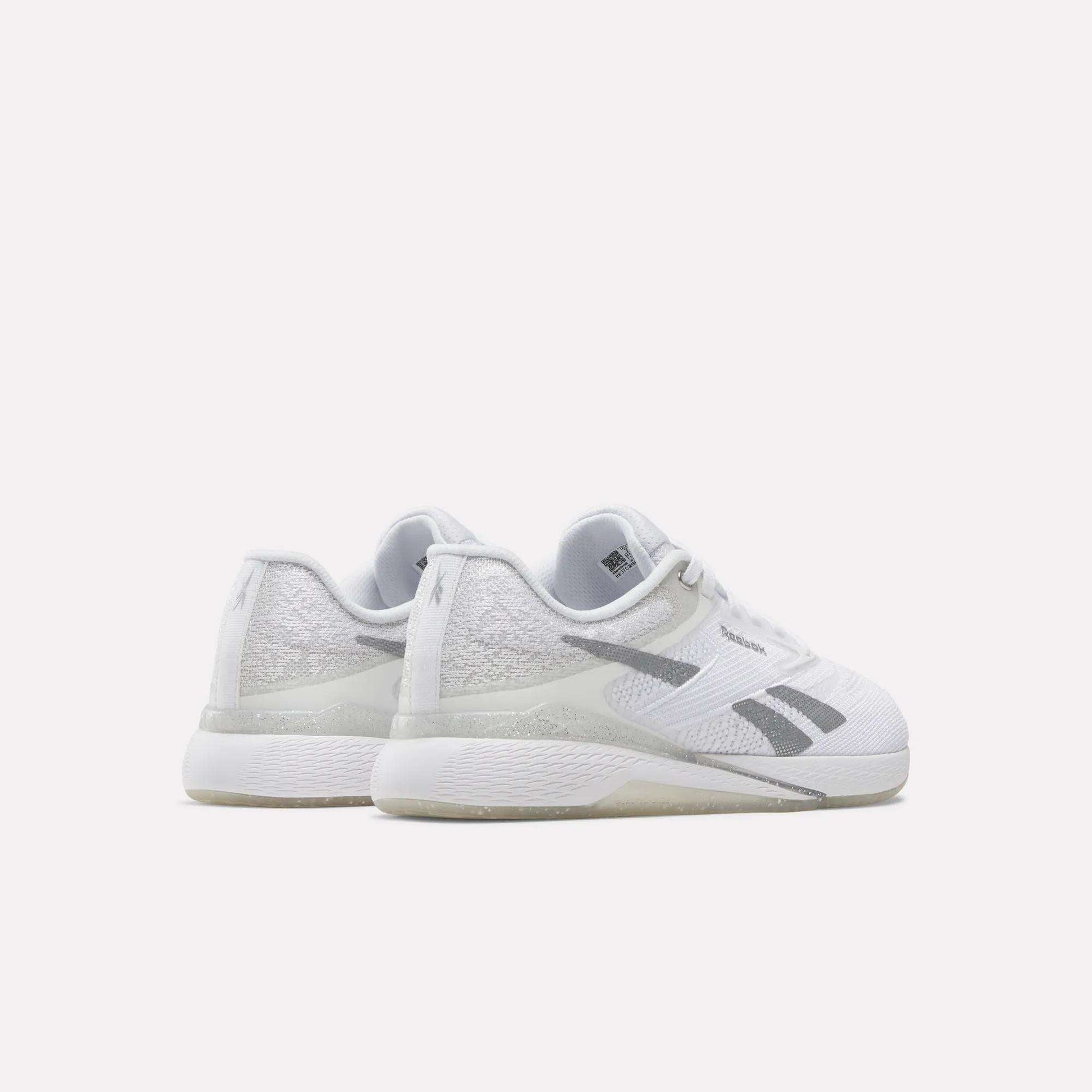 A pair of Reebok Women's Nano X5 Training Shoes, featuring a white design with gray accents and textured details, is positioned on a white surface to display the back and side views.