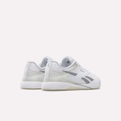 A pair of Reebok Women's Nano X5 Training Shoes, featuring a white design with gray accents and textured details, is positioned on a white surface to display the back and side views.