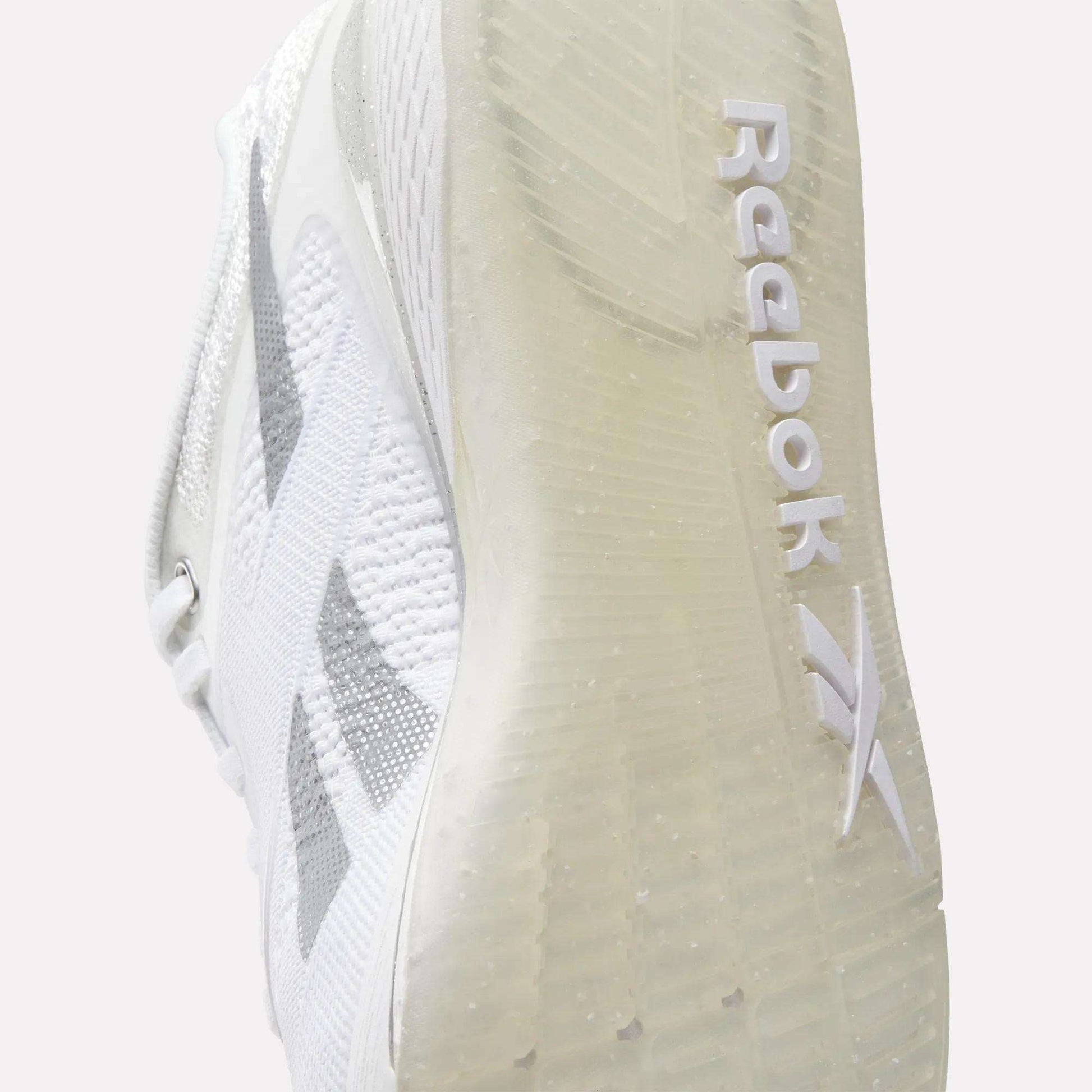 Close-up of the sole of Reebok Women's Nano X5 Training Shoes, highlighting the Reebok logo and textured grip on the transparent sole. The upper features a subtle gray design for style and comfort.