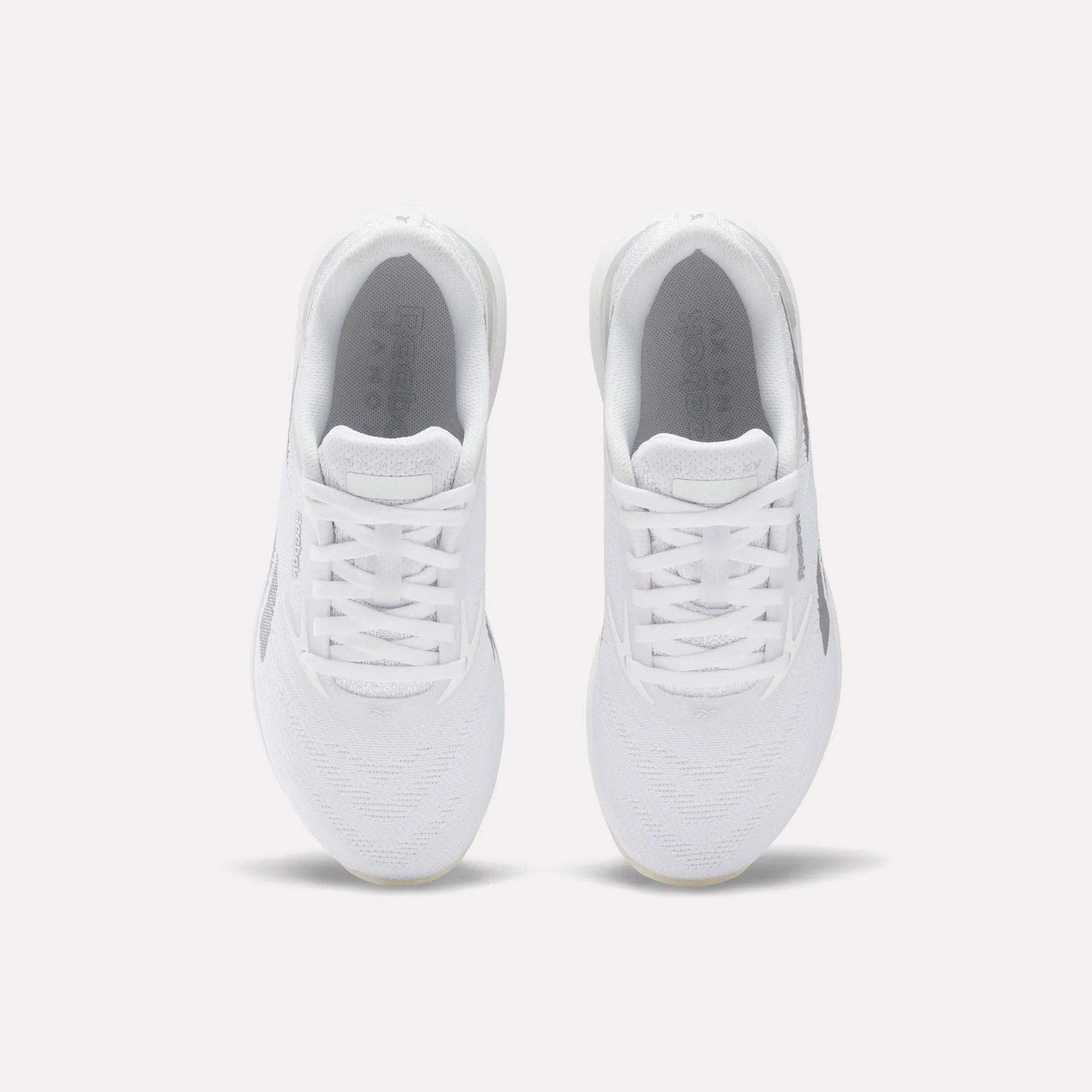 A pair of comfortable white Reebok Women's Nano X5 Training Shoes viewed from above on a plain light background, highlighting the laces, mesh texture, and Reebok branding on the insoles.