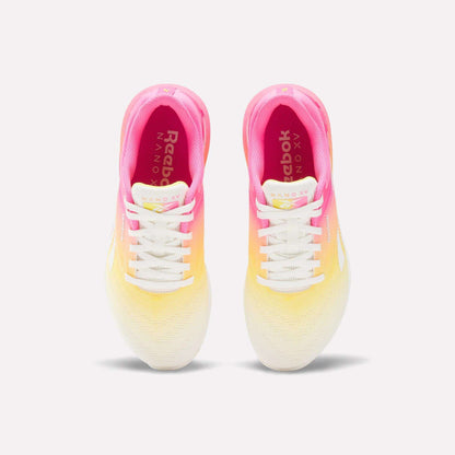 A pair of Reebok Women's Nano X5 Training Shoes shown from above, with a gradient design fading from pink at the heel to yellow midfoot and white at the toe, white laces, and Reebok branding on the insoles.