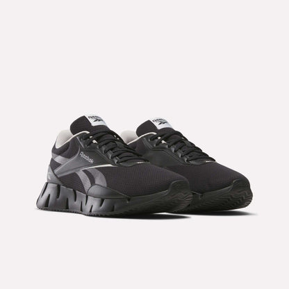A pair of black Reebok Zig Dynamica STR running shoes with white accents, FuelFoam midsole, thick segmented soles, and mesh uppers is displayed against a plain white background.